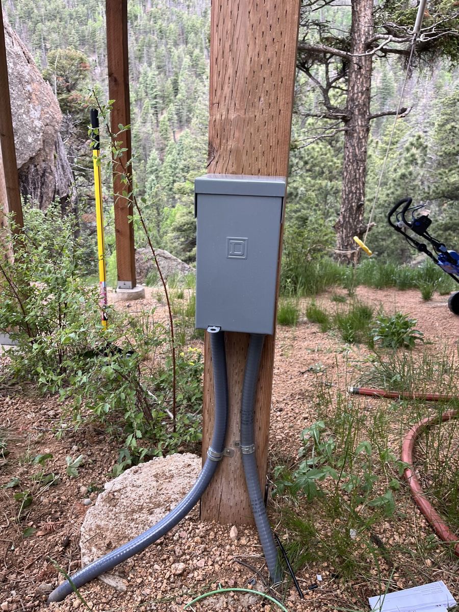 Disconnect box mounted on wood post in landscaped backyard with mountain view