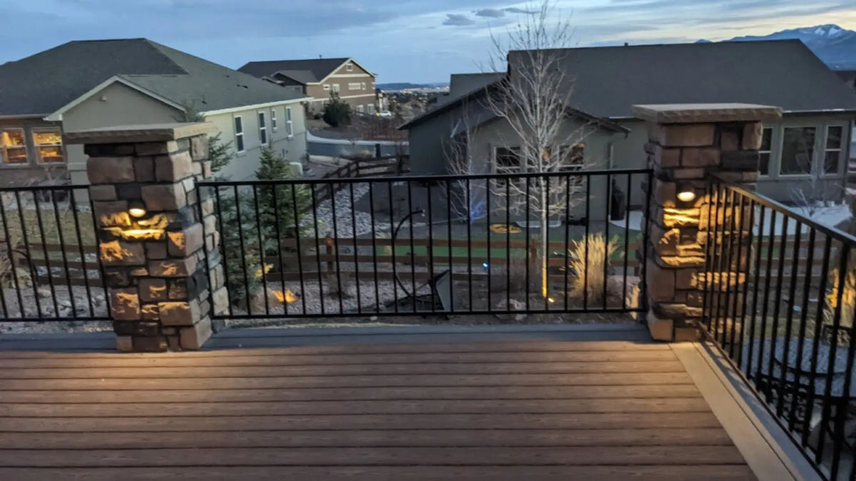 Backyard deck with stone column lights illuminated at twilight, mountain backdrop